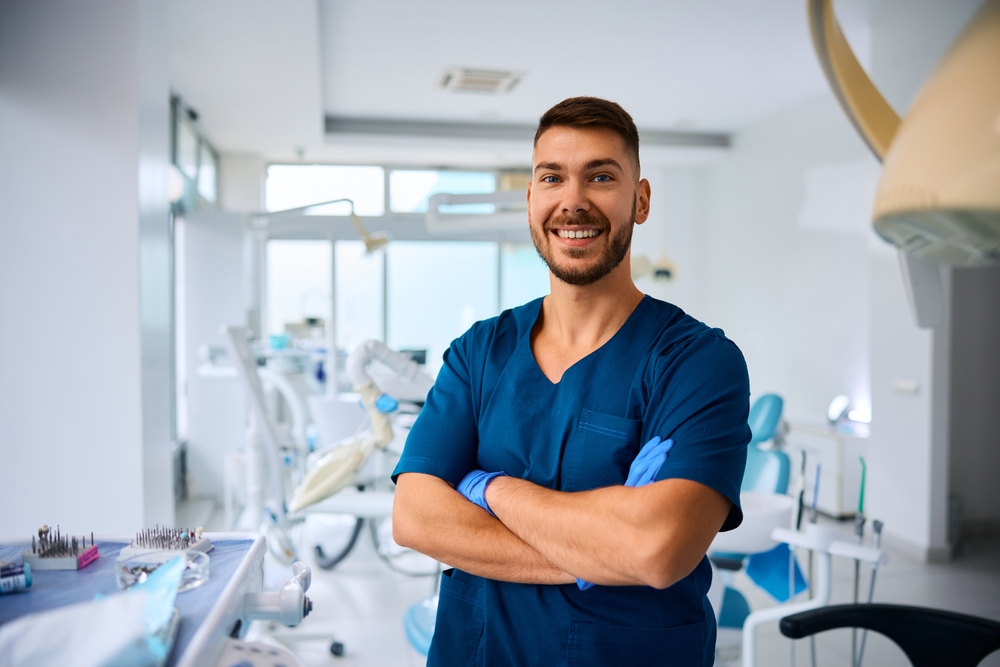 Confident Dentist in Modern Clinic – Dental Practice Valuation Smiling dentist standing confidently in a bright, modern dental office representing success after a professional business assessment – Dental Practice Valuation